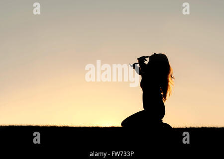 Une silhouette d'une femme à genoux avec ses mains en l'air, en priant, en remerciant, et l'abandon à Dieu. Banque D'Images