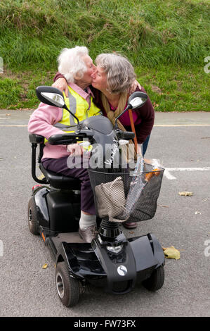 Femme âgée assise dans son scooter de mobilité s'embrasser et s'étreindre sa garde Banque D'Images