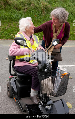 Femme âgée assise dans son scooter de mobilité de parler à sa garde Banque D'Images