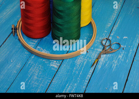 Fils multicolores, hoop et ciseaux pour la couture et broderie sur une table en bois bleu Banque D'Images