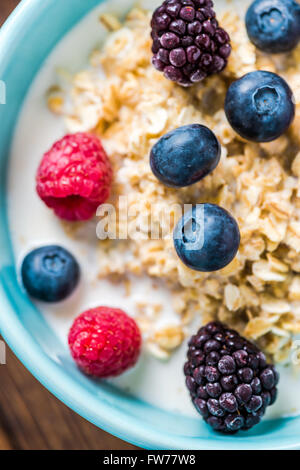 Bol avec de petits fruits rouges et de porridge, vue du passage sur table rustique en bois. Banque D'Images