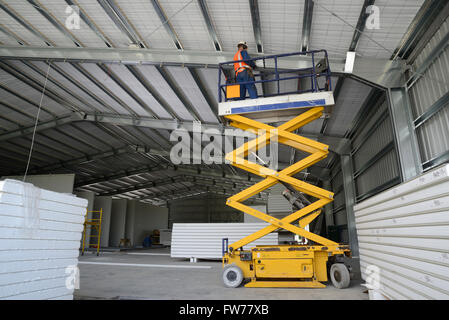 Un constructeur travaille à partir de la cage sur une table élévatrice à poutres apparentes lors de l'attachement dans un nouveau bâtiment commercial. Banque D'Images