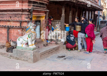 Bhaktapur, Népal. Les femmes attendaient leur tour en fonction d'un robinet d'eau. Garde des Lions un quartier de culte hindou sur la gauche. Banque D'Images