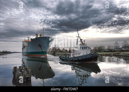 Remorqueur tirant une grande Maritime cargo sur un canal en bateau de navigation au crépuscule Banque D'Images