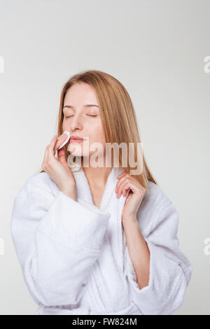 Femme en peignoir face nettoyage avec un coton isolé sur fond blanc Banque D'Images