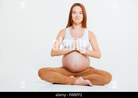 Femme enceinte en méditant sur le plancher isolé sur fond blanc Banque D'Images