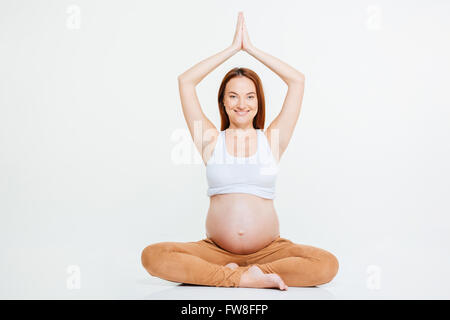 Smiling pregnant woman doing yoga exercice sur le plancher isolé sur fond blanc Banque D'Images