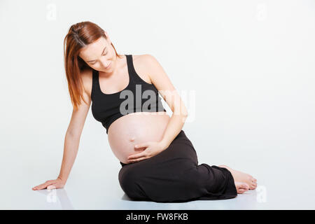 Jeune femme enceinte assis sur le plancher isolé sur fond blanc Banque D'Images
