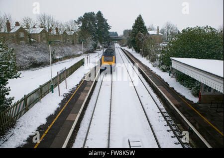 Les voies de train de partir dans de la distance avec un train intercity sur l'une ou l'autre vient juste de partir ou arriver à une station dans les Cotswolds au Royaume-Uni. La grande ligne de trains de l'ouest a été couverte dans une couverture de neige et la neige sur les pistes et les conditions de gel avec de la glace dans cette scène d'hiver au Royaume-Uni, rendre les voyages affaires difficile pour le moteur. Banque D'Images