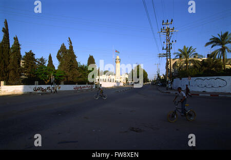 Une scène sur les toits de la ville de Gaza, montrant le haut d'un minaret et les drapeaux palestiniens par le haut et à proximité tlegraph poteaux, un enfant dans la rue sur leurs vélos et tous semble calme comme le soleil se couche. Banque D'Images