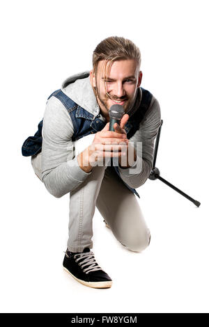 Studio portrait d'un homme chantant avec microphone isolé sur fond blanc, un beau jeune homme aux cheveux blonds le chant avec dri Banque D'Images