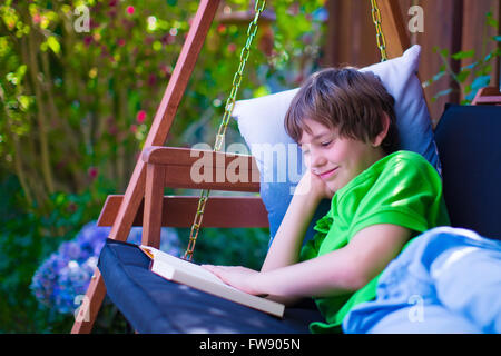 Happy school boy lire un livre dans la cour. Enfant dans un jardin relaxant avec rotation des livres. Lire pour les enfants pendant les vacances d'été. Banque D'Images