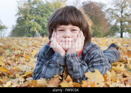 Petit garçon couché dans les feuilles d'automne Banque D'Images