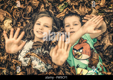 Deux enfants se trouvant dans les feuilles et de jouer Banque D'Images