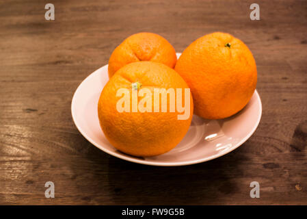 Trois oranges dans Bol en porcelaine blanche sur table en bois Banque D'Images