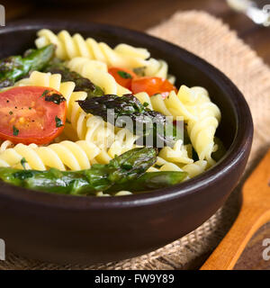 Asperges vertes cuites au four, tomate cerise et salade de pâtes rotini servi dans bol rustique, photographiés sur des meubles en bois avec éclairage naturel Banque D'Images