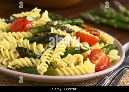 Asperges vertes cuites au four, tomate cerise et salade de pâtes rotini servi sur assiette, photographiée en bois foncé avec lumière naturelle Banque D'Images