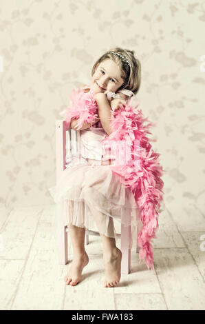 Jeune fille en robe de soirée assis sur chaise en bois holding feather foulard et posing Banque D'Images