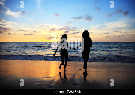 Deux jeunes femmes heureux de marcher sur une plage de la mer au coucher du soleil tropical Banque D'Images
