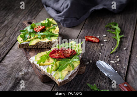 Toast avec du fromage de chèvre en bonne santé, d'avocat, roquette et tomates séchées au soleil sur une table en bois rustique. Selective focus Banque D'Images