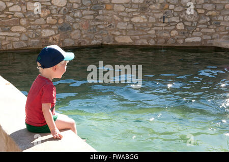 Tout-petit assise sur le bord d'une piscine avec ses pieds se balançant dans l'eau Banque D'Images