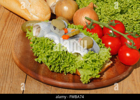 Rouleaux de poisson avec du hareng hareng mariné, aigre, garni de laitue, tomate et des cornichons sur une planche en bois Banque D'Images