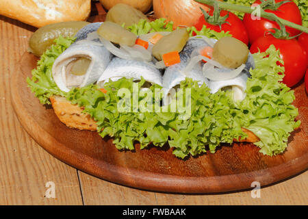 Rouleaux de poisson avec du hareng hareng mariné, aigre, garni de laitue, tomate et des cornichons sur une planche en bois Banque D'Images