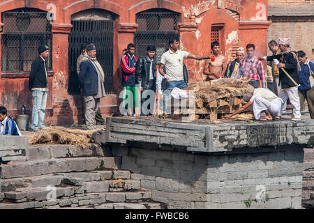 Le Népal, Pashupatinath. La crémation étapes. Allumer le feu sous le cadavre, enveloppé dans un drap blanc, tandis qu'un membre de la famille Banque D'Images