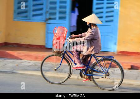 Woman riding a bike dans les rues de la vieille ville de Hoi An, Vietnam, Asie Banque D'Images