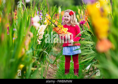 Little girl holding glaïeul fleurs''. Préparation de l'enfant des fleurs fraîches dans le jardin. Les enfants le jardinage en automne. Banque D'Images