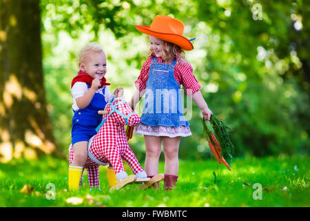 Petit garçon et fille habillé en cowboy et cowgirl Playing with toy cheval à bascule en position de stationnement. Les enfants jouent à l'extérieur. Banque D'Images