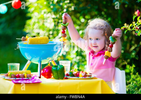 Les enfants de la viande cuisson. Camping en famille et profiter du barbecue. Petite fille à préparer un barbecue biftecks, brochettes et le maïs. Banque D'Images