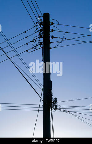 Un pôle realiser les fils pour la compagnie d'électricité traverse la campagne dans la lumière du soir avec l'avertissement de danger posté sur un signe à sa base. Banque D'Images