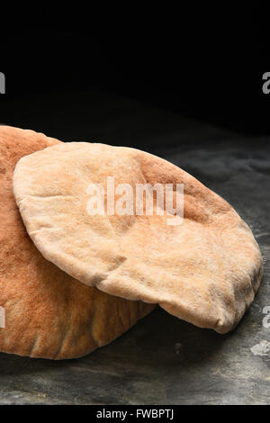 Gros plan vertical des miches de pain pita de blé entier sur une surface en ardoise et fond noir. Banque D'Images