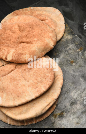 Gros plan vertical des miches de pain pita de blé entier sur une surface en ardoise grise et fond noir. Banque D'Images