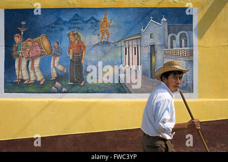Homme marchant local devant un mur haletant dans San Juan La Laguna, Solola, Guatemala. Peinture art traditionnels mayas Santiago UN Banque D'Images