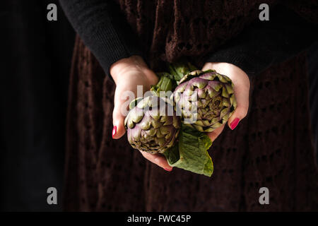 Mains tenant artichauts frais Banque D'Images