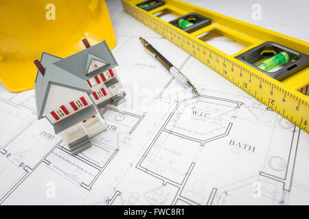 Maison modèle, niveau, casque et un crayon posé sur un plan de maison personnalisé. Banque D'Images