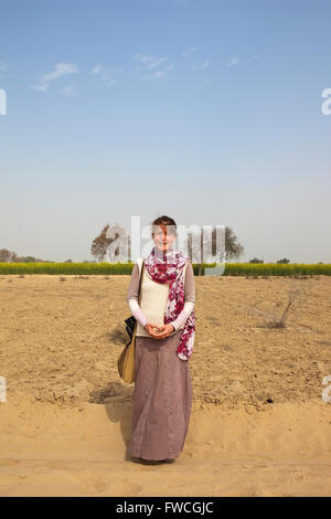 Une dame de l'promenades le long d'une piste poussiéreuse entre la floraison de la moutarde des champs dans Abohar, Ferozepur, district rural du Rajasthan Banque D'Images