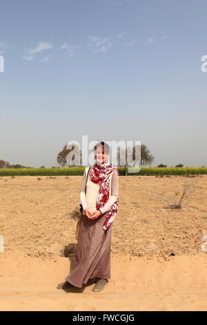 Une dame de l'promenades le long d'une piste poussiéreuse entre la floraison de la moutarde des champs dans Abohar, Ferozepur, district rural du Rajasthan Banque D'Images