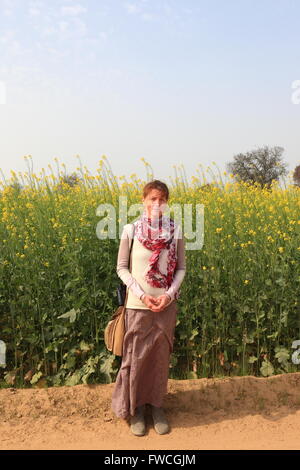 Une dame de l'promenades le long d'une piste poussiéreuse entre la floraison de la moutarde des champs dans Abohar, Ferozepur, district rural du Rajasthan Banque D'Images