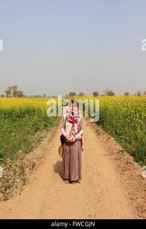 Une dame de l'promenades le long d'une piste poussiéreuse entre la floraison de la moutarde des champs dans Abohar, Ferozepur, district rural du Rajasthan Banque D'Images