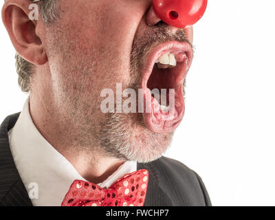 Photo Gros plan d'un homme en costume avec un nez en caoutchouc rouge et noeud papillon rouge brillant crier au sommet de ses poumons. Banque D'Images