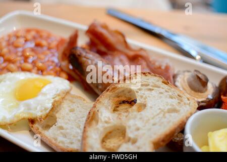 Un petit-déjeuner chaud avec du pain grillé, bacon, œuf frit, des saucisses, des haricots blancs, de champignon et de beurre - filtre appliqué