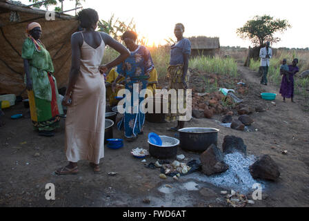 Lacekocot, Pader, en Ouganda. Un groupe de femmes des tribus Acholi cuisent à feu ouvert alors que le soleil se couche sur un camp de réfugiés en Afrique.Les femmes sont la cuisson dans de grands pots sur fond de coucher de soleil sur huttes de boue. Banque D'Images