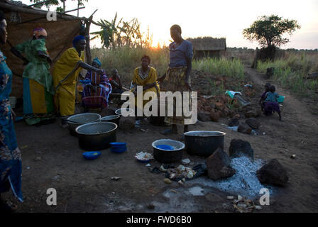 Lacekocot, Pader, en Ouganda. Un groupe de femmes des tribus Acholi cuisent à feu ouvert alors que le soleil se couche sur un camp de réfugiés en Afrique.Les femmes sont la cuisson dans de grands pots sur fond de coucher de soleil sur huttes de boue. Banque D'Images