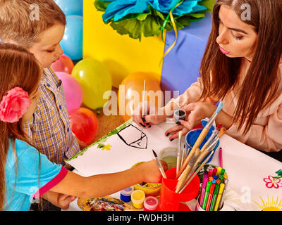 Les enfants avec l'enseignant femme peinture sur papier à la maternelle . Banque D'Images