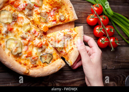 Cueillette à la main Tranche de pizza savoureuse allongé sur table en bois Banque D'Images