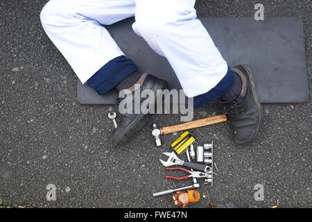 Mécanicien automobile avec ses jambes coller dehors et d'outils à ses pieds Banque D'Images