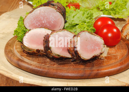 Médaillons de filet de porc, viande, enrobé de bacon, grillé et garni de laitue et tomates sur une planche en bois Banque D'Images